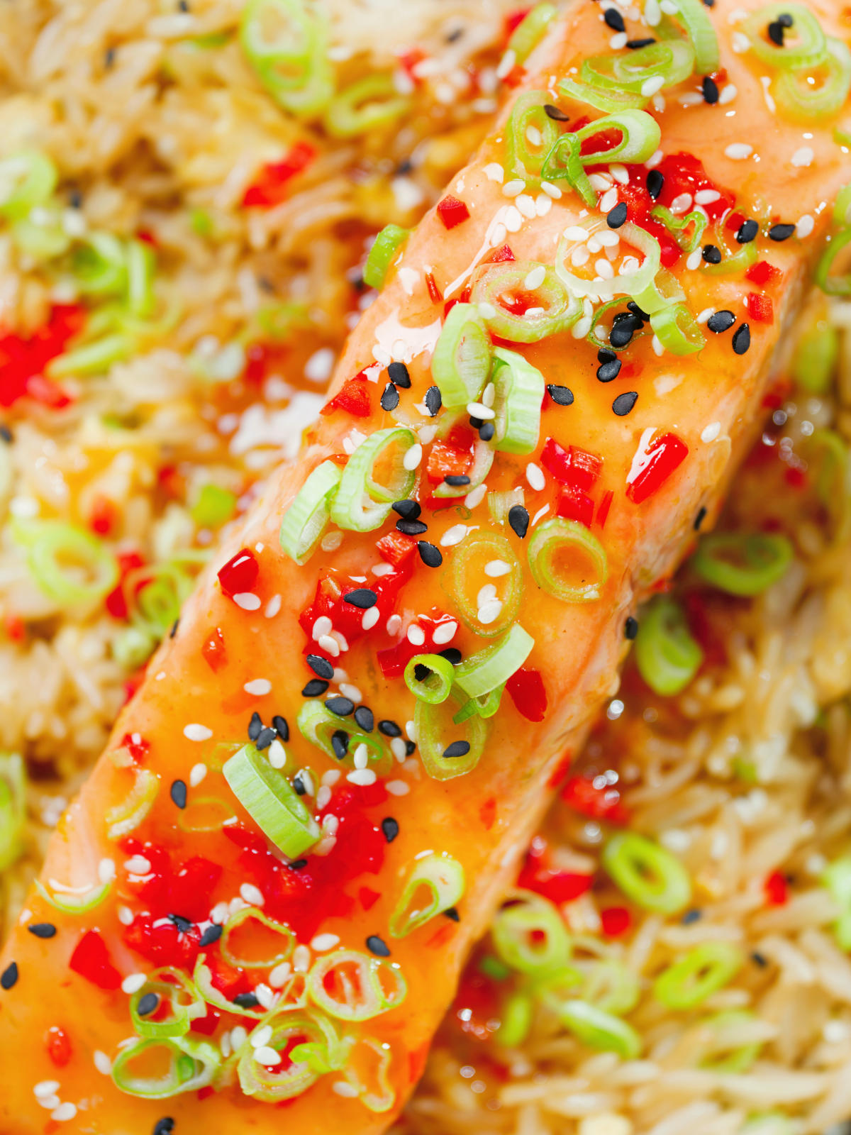 Overhead close-up sweet chilli sauce baked salmon with egg fried rice, fresh chilli and spring onions.