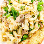 Close-up overhead tinned mackerel, tenderstem broccoli pasta served with garlic bread.