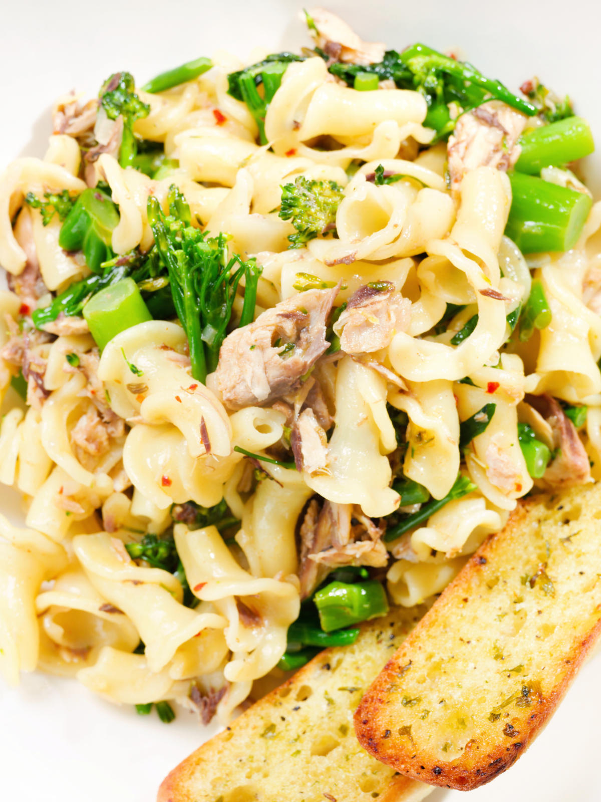 Close-up overhead tinned mackerel, tenderstem broccoli pasta served with garlic bread.