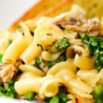 Close-up tinned mackerel, tenderstem broccoli pasta served with garlic bread.
