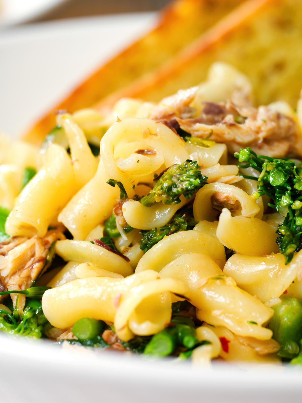 Close-up tinned mackerel, tenderstem broccoli pasta served with garlic bread.