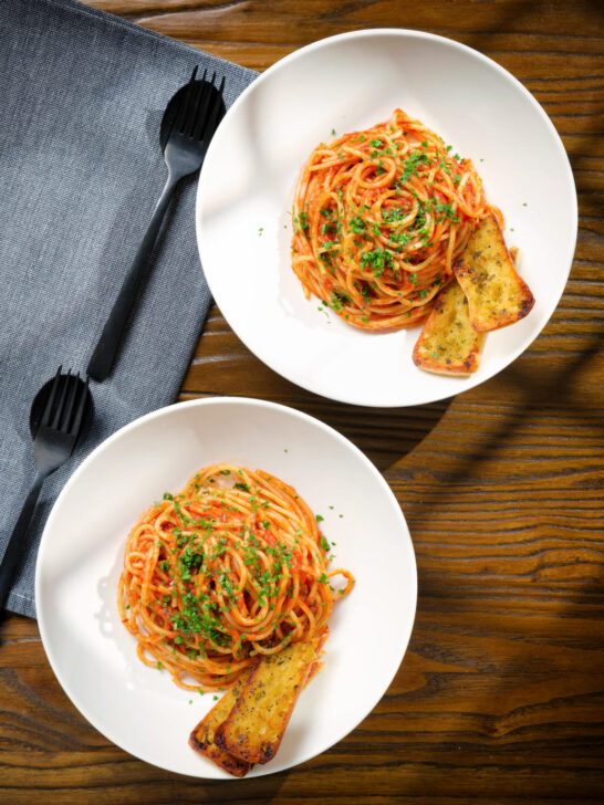 Overhead tomato and anchovy pasta served with garlic bread.