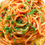 Close-up overhead tomato and anchovy pasta served with garlic bread.