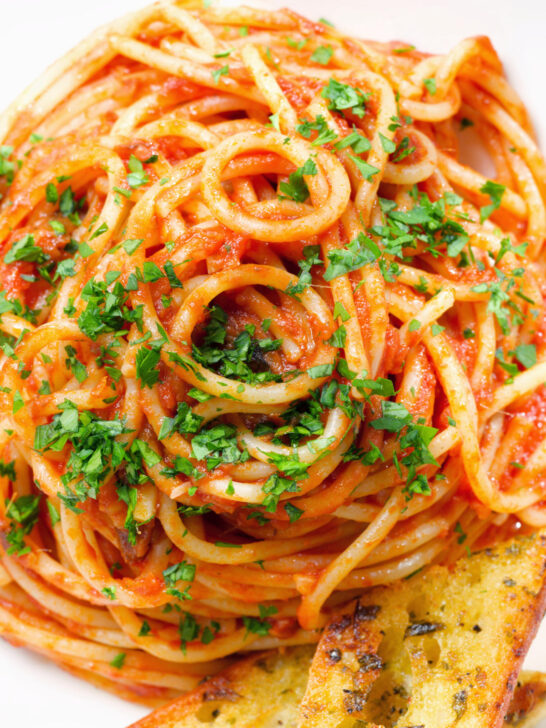 Close-up overhead tomato and anchovy pasta served with garlic bread.