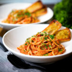 Tomato and anchovy pasta (spaghetti) served with garlic bread and fresh parsley.