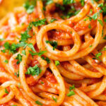 Close-up tomato and anchovy pasta served with garlic bread.