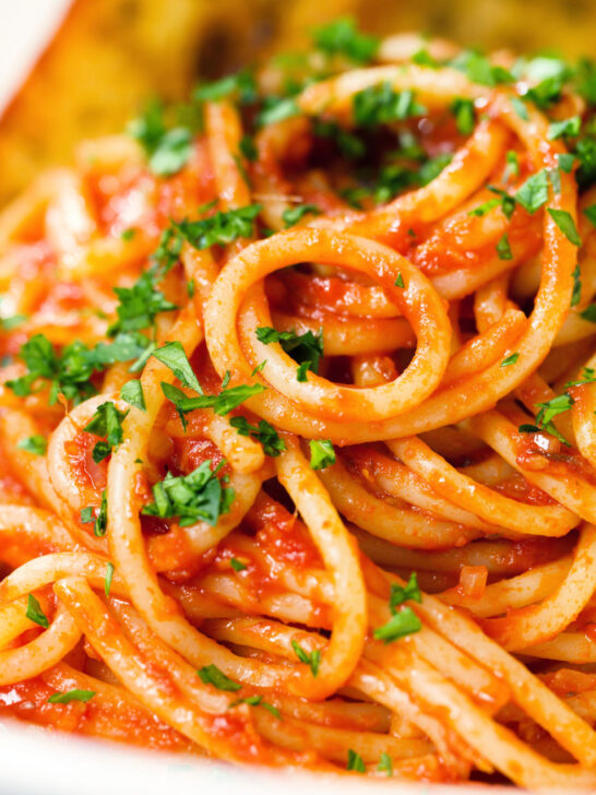 Close-up tomato and anchovy pasta served with garlic bread.