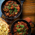 Overhead Keralan style beef curry served with fresh coriander and naan bread.