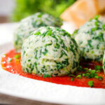 Close-up Italian Malfatti (spinach and ricotta dumplings) with tomato sauce and garlic bread.