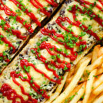 Overhead close-up Polish cheese and mushroom zapiekanka open sandwich served with ketchup and fries.