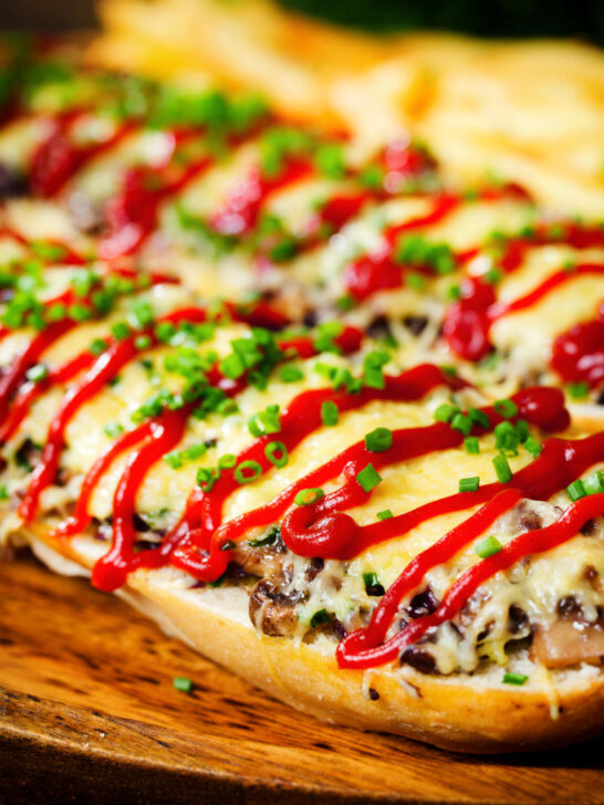 Close-up Polish cheese and mushroom zapiekanka open sandwich served with ketchup and fries.