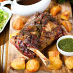 Slow roasted lamb shoulder with roast potatoes, homemade mint sauce, gravy served on a board.