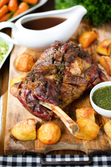Slow roasted lamb shoulder with roast potatoes, homemade mint sauce, gravy served on a board.