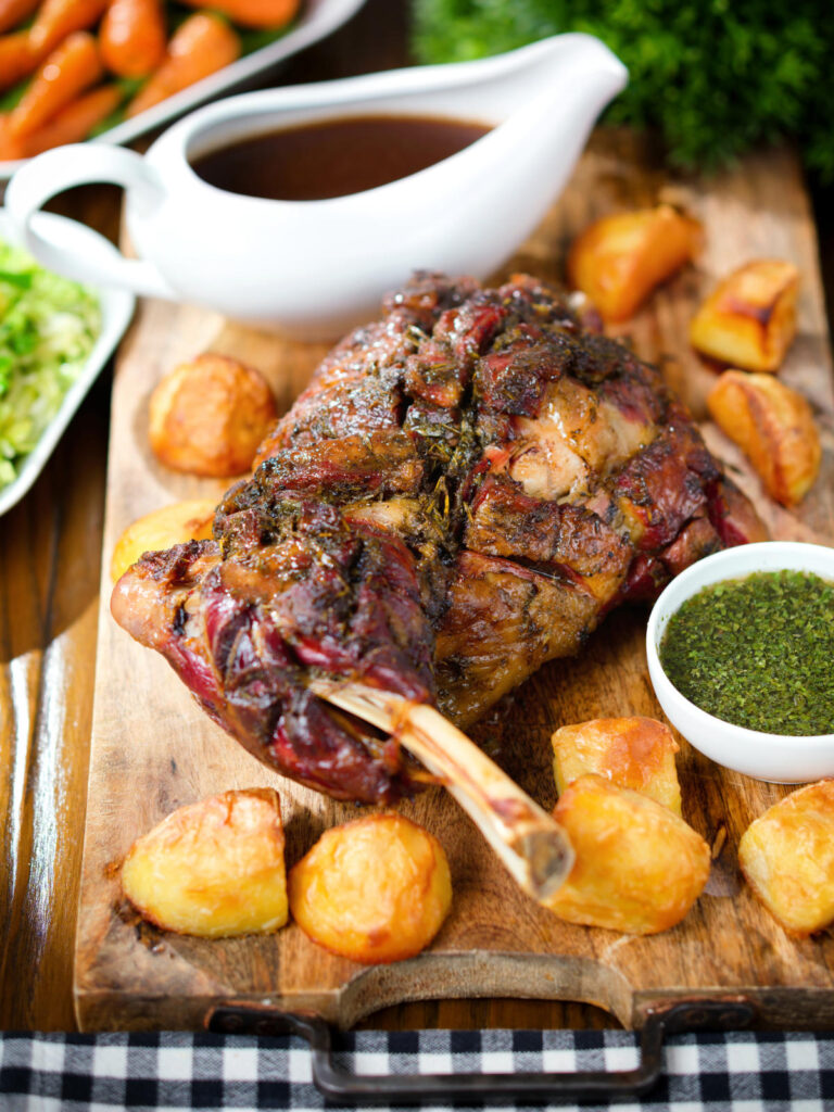 Slow roasted lamb shoulder with roast potatoes, homemade mint sauce, gravy served on a board.