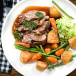 Overhead Sunday lunch of slow roasted lamb shoulder with roast potatoes, veggies, mint sauce and gravy.