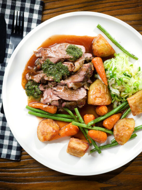 Overhead Sunday lunch of slow roasted lamb shoulder with roast potatoes, veggies, mint sauce and gravy.