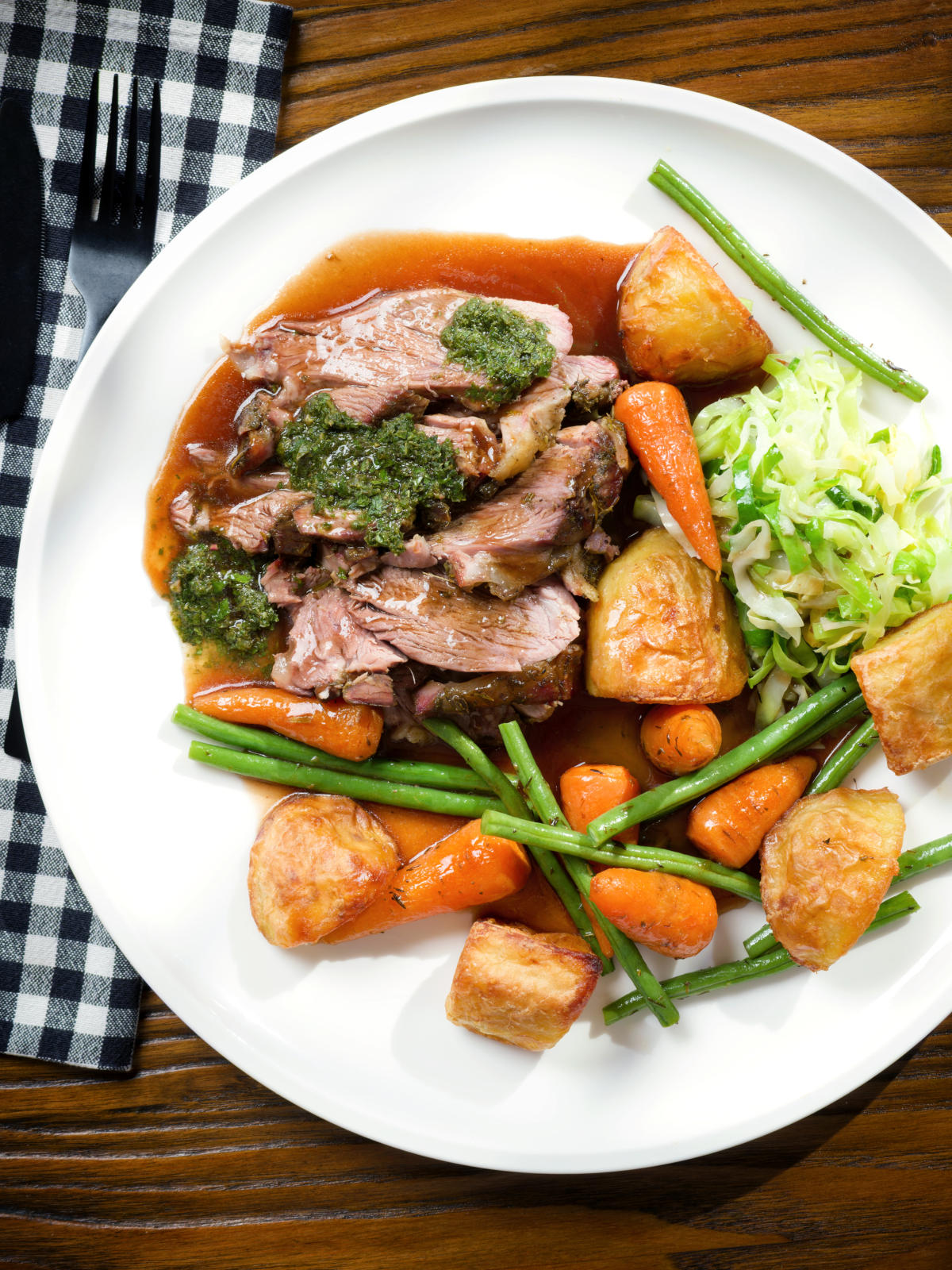 Overhead Sunday lunch of slow roasted lamb shoulder with roast potatoes, veggies, mint sauce and gravy.