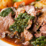 Close-up Sunday lunch of slow roasted lamb shoulder with roast potatoes, veggies, mint sauce and gravy.