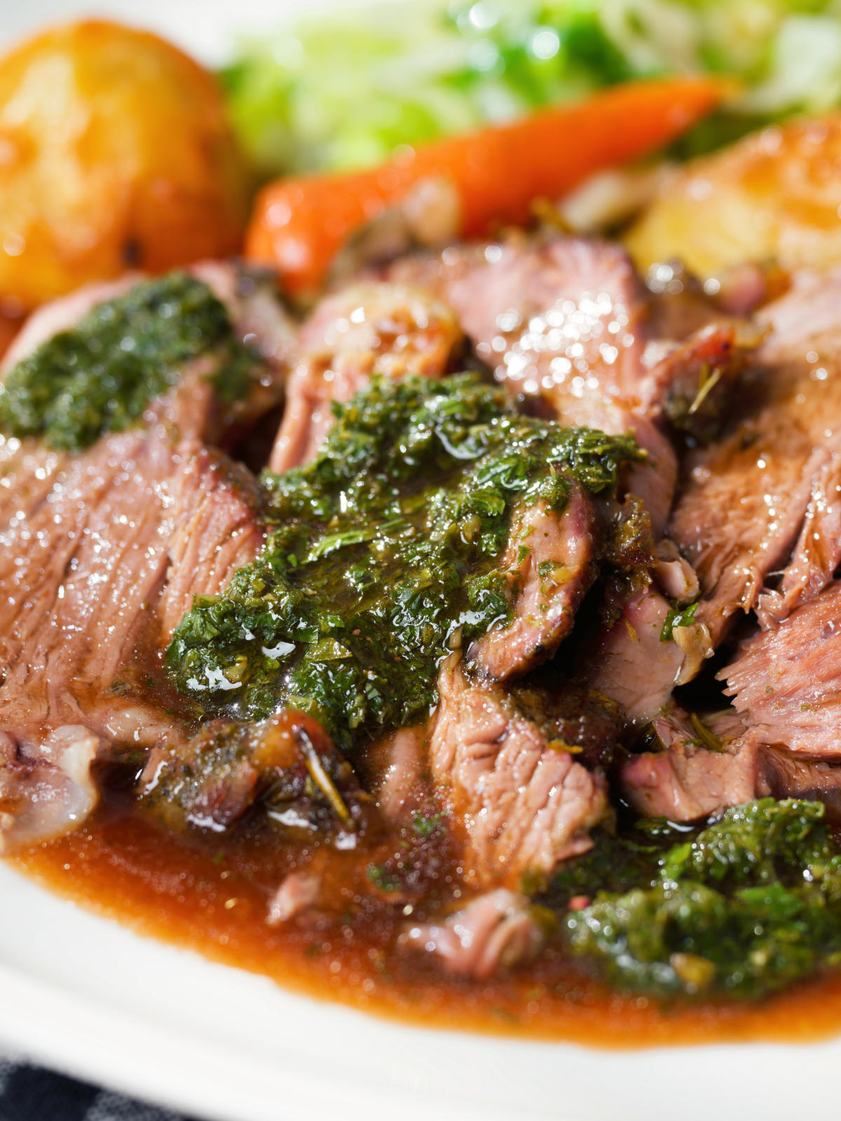 Close-up Sunday lunch of slow roasted lamb shoulder with roast potatoes, veggies, mint sauce and gravy.