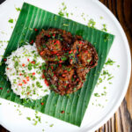 Vegan mushroom rendang curry served with rice on a banana leaf.