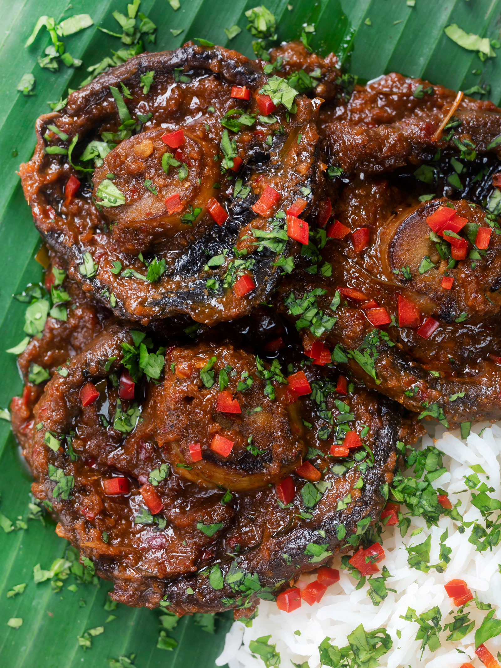 Overhead close-up vegan mushroom rendang curry served with rice, fresh chilli and coriander.