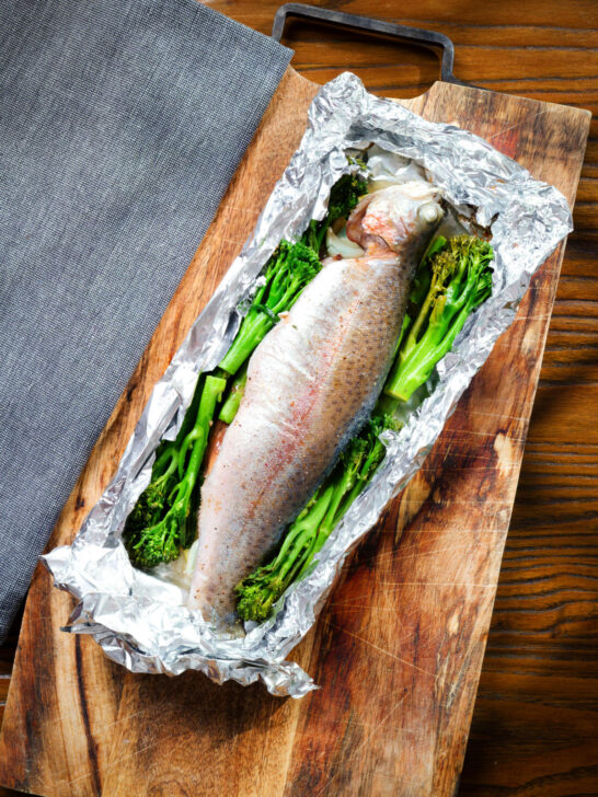 Overhead whole baked fish (rainbow trout) cooked in foil with asparagus and tenderstem broccoli.