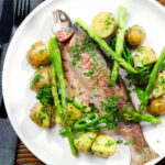 Overhead baked fish (rainbow trout) that was cooked in foil with asparagus and tenderstem broccoli, served with buttered potatoes.