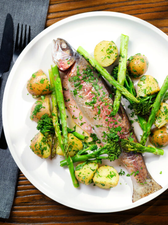 Overhead baked fish (rainbow trout) that was cooked in foil with asparagus and tenderstem broccoli, served with buttered potatoes.