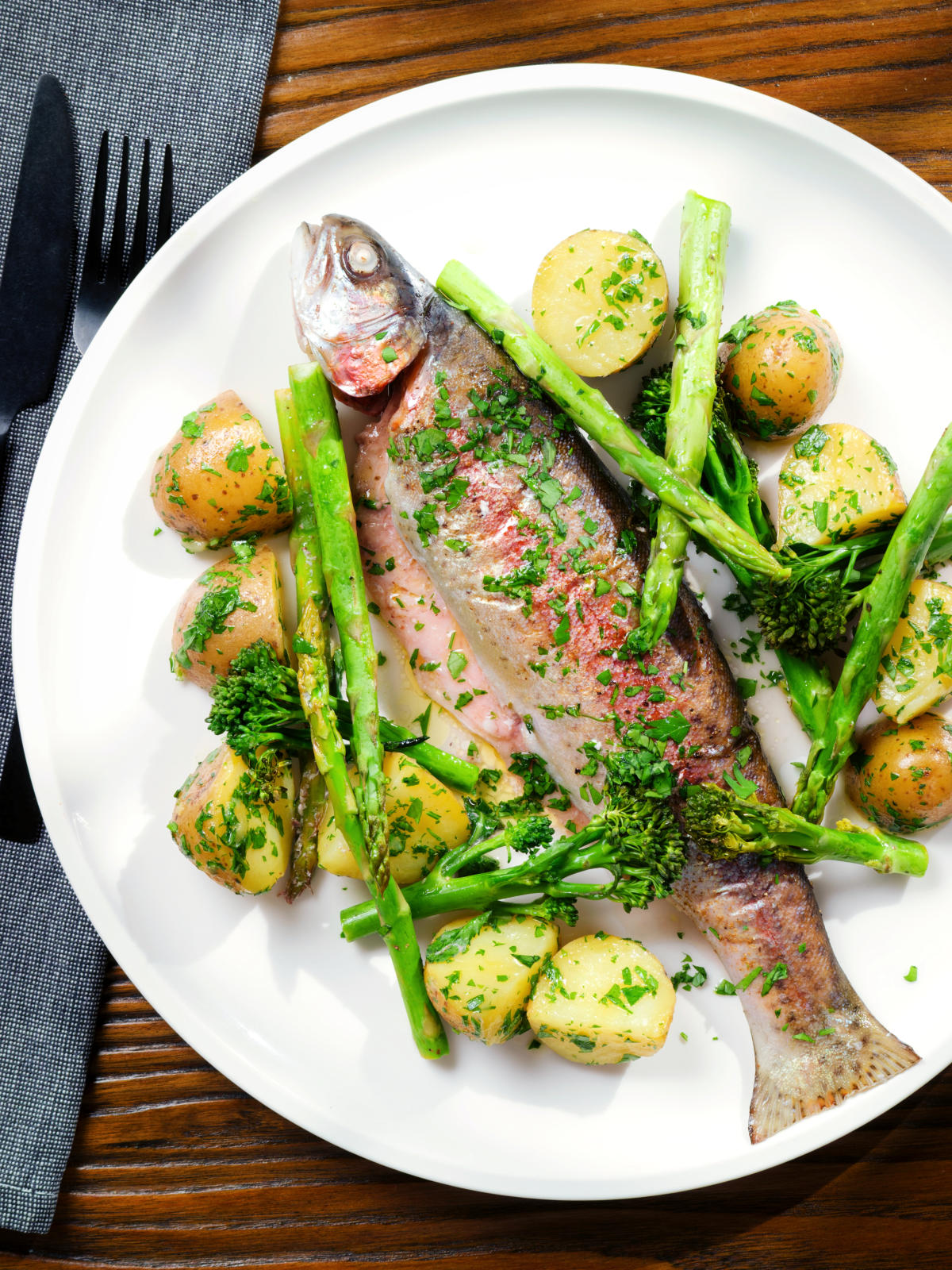 Overhead baked fish (rainbow trout) that was cooked in foil with asparagus and tenderstem broccoli, served with buttered potatoes.