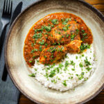 Overhead Indian chicken kolhapuri curry served with rice and coriander.