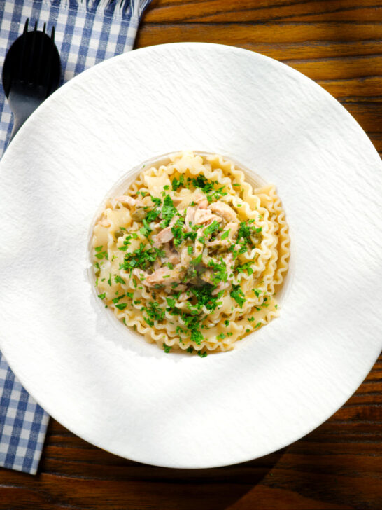 Overhead lemon and caper chicken piccata pasta (malfadine) garnished with fresh parsley.
