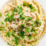 Close-up overhead lemon and caper chicken piccata pasta (malfadine) garnished with fresh parsley.