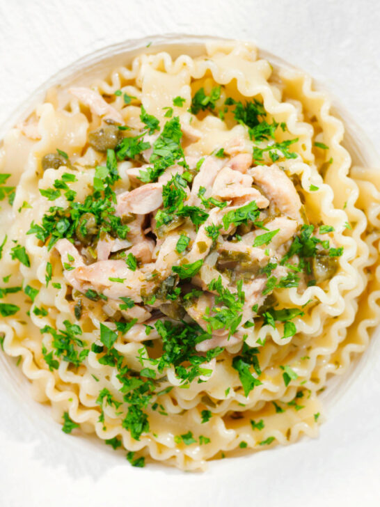 Close-up overhead lemon and caper chicken piccata pasta (malfadine) garnished with fresh parsley.