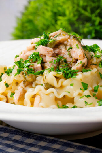 Close-up lemon and caper chicken piccata pasta (malfadine) garnished with fresh parsley.
