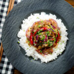 Overhead Chinese Xinjiang lamb stir fry with cumin, dried chillies and red onion served with rice.