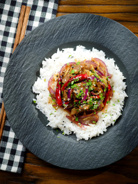 Overhead Chinese Xinjiang lamb stir fry with cumin, dried chillies and red onion served with rice.