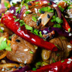 Close-up Chinese Xinjiang lamb stir fry with cumin, dried chillies and red onion.
