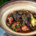 Coq au vin, chicken legs braised in red wine with vegetables and bacon.