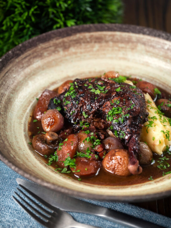Coq au vin, chicken legs braised in red wine with vegetables and bacon.