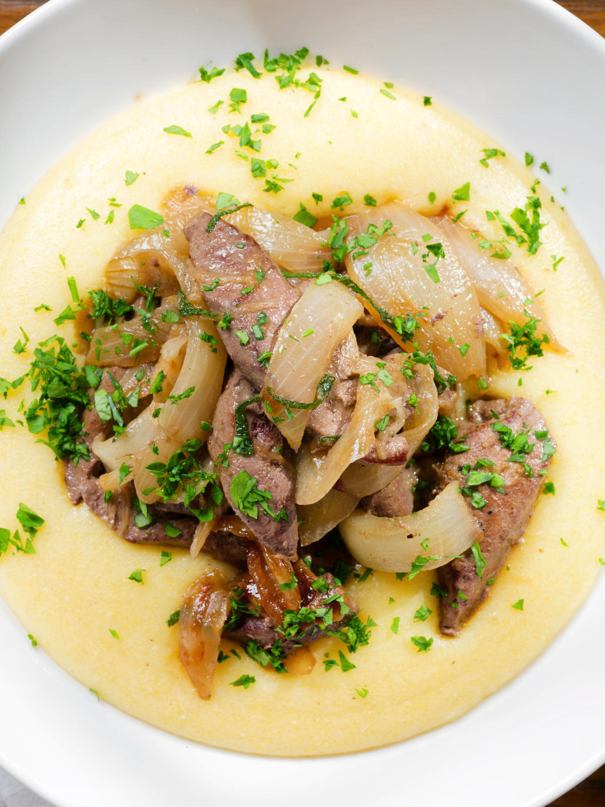 Overhead close-up Fegato alla Veneziana (Italian fried liver and onions) served with polenta.