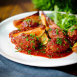 Soutzoukakia (Greek beef meatballs) in a red wine and tomato sauce with salad and potato wedges.