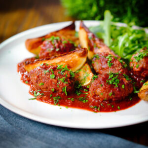 Soutzoukakia (Greek beef meatballs) in a red wine and tomato sauce with salad and potato wedges.