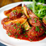 Soutzoukakia (Greek beef meatballs) in tomato sauce with salad and potato wedges.