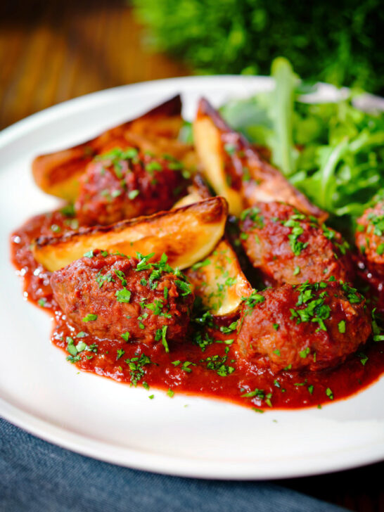 Soutzoukakia (Greek beef meatballs) in tomato sauce with salad and potato wedges.