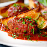 Soutzoukakia (Greek beef meatballs) in tomato sauce with potato wedges.