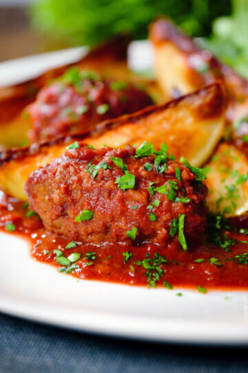 Soutzoukakia (Greek beef meatballs) in tomato sauce with potato wedges.