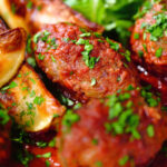 Close-up Soutzoukakia (Greek beef meatballs) in tomato sauce with baked potato wedges.