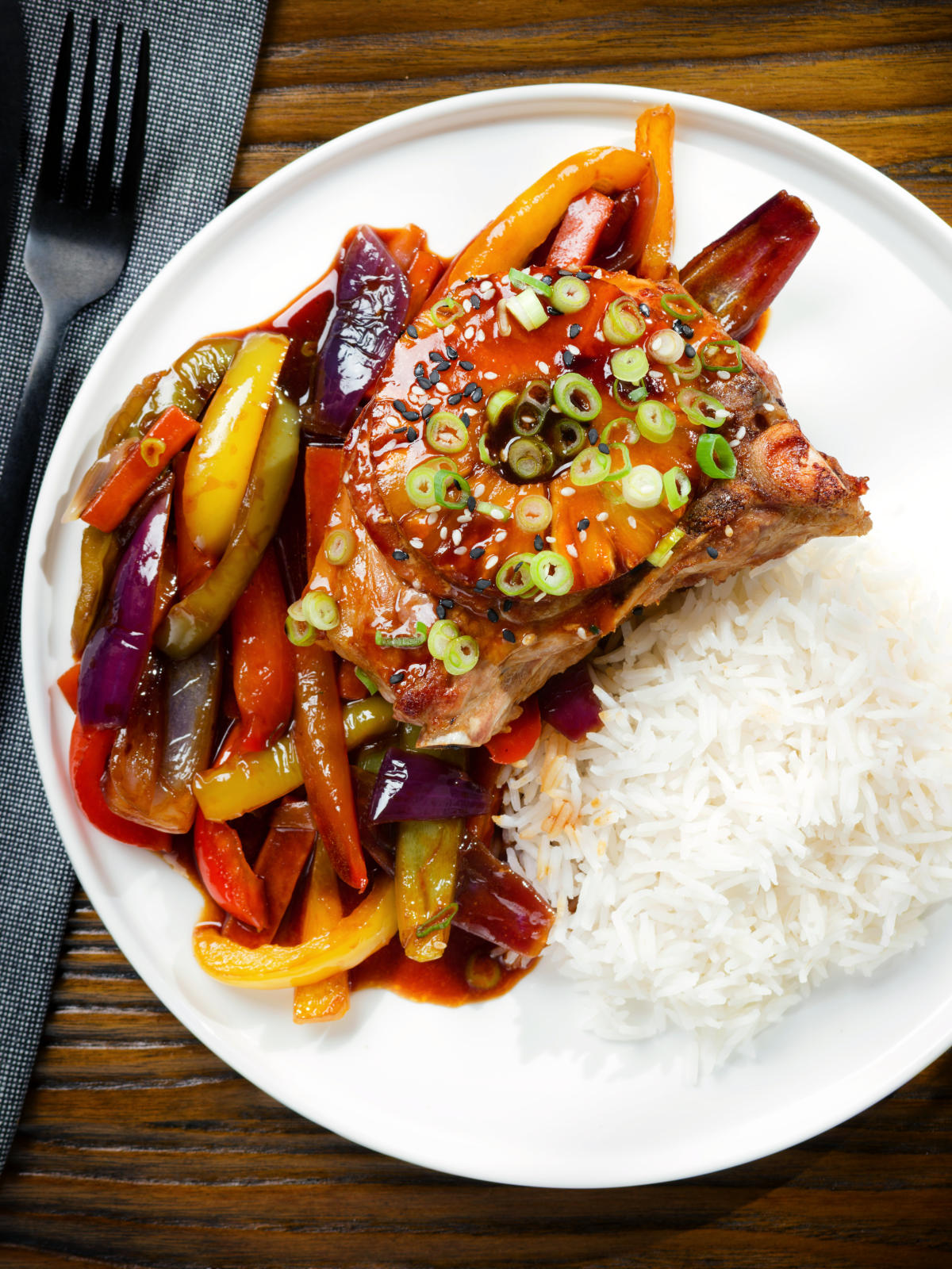Overhead sweet and sour pork chops with peppers, red onion and pineapple, served with rice.