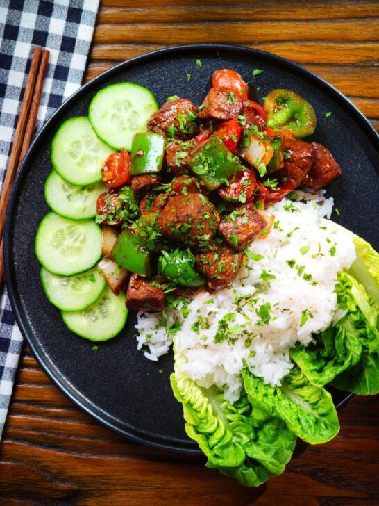 Overhead Vietnamese shaking beef (bò lúc lắc) served with cucumber, jasmine rice and lettuce.