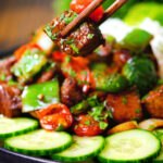 Vietnamese shaking beef (bò lúc lắc) served with cucumber, rice and lettuce being picked up with chopsticks.